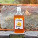Botella de Miel natural pura de abejas Apícola Biomiel de 500g, con dosificador, sobre tablones rústicos y panal de abejas al fondo.